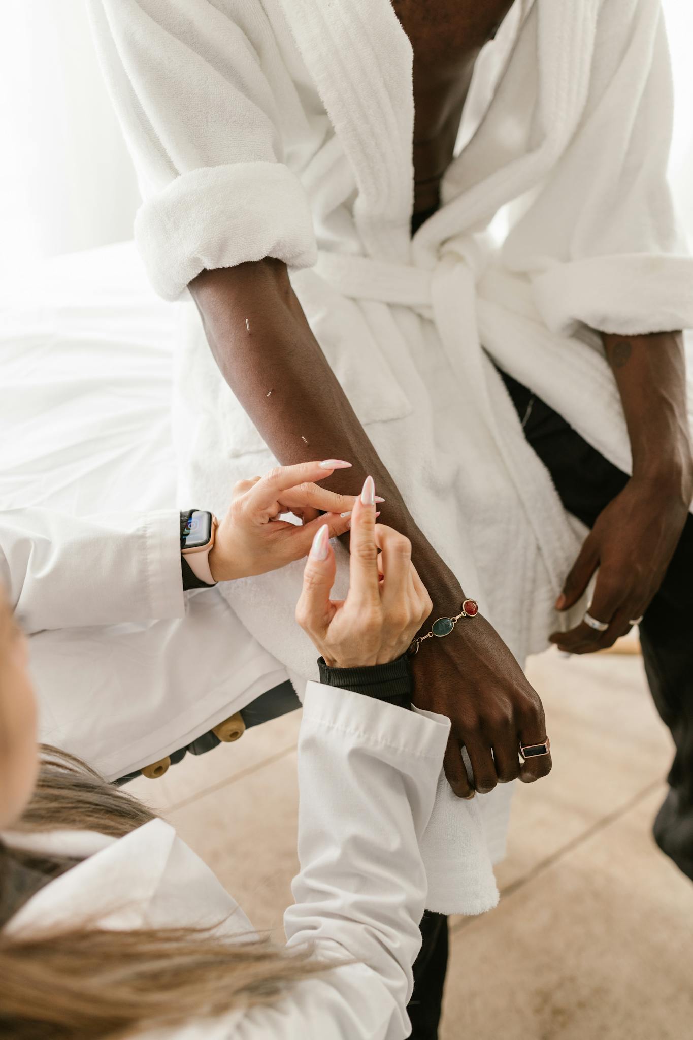 Close-up of acupuncture session showing therapist placing needles in patient's arm for wellness.